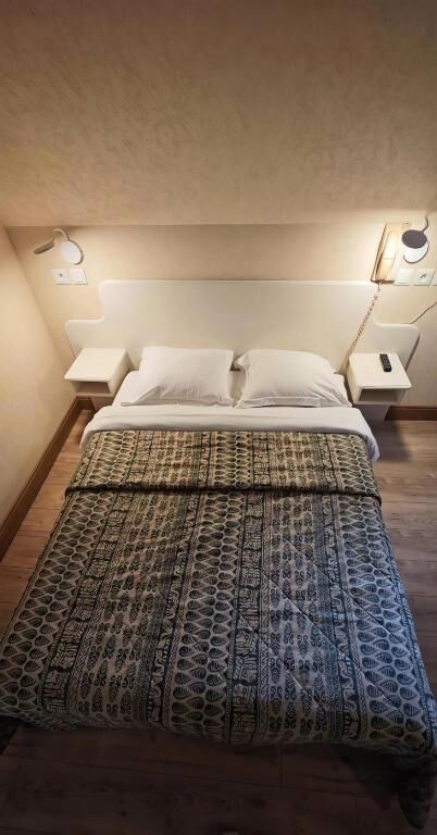Grand lit avec tables de chevet et liseuses dans une chambre de l'Hotel De France